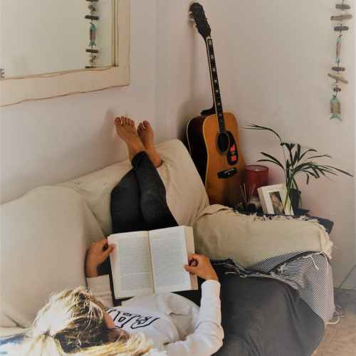woman reading book while lying on sofa